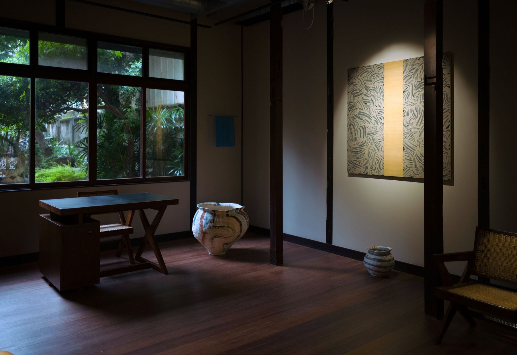 A room with windows onto a garden, a desk, ceramic jars on the floor and Richard Long's mud work on the wall.