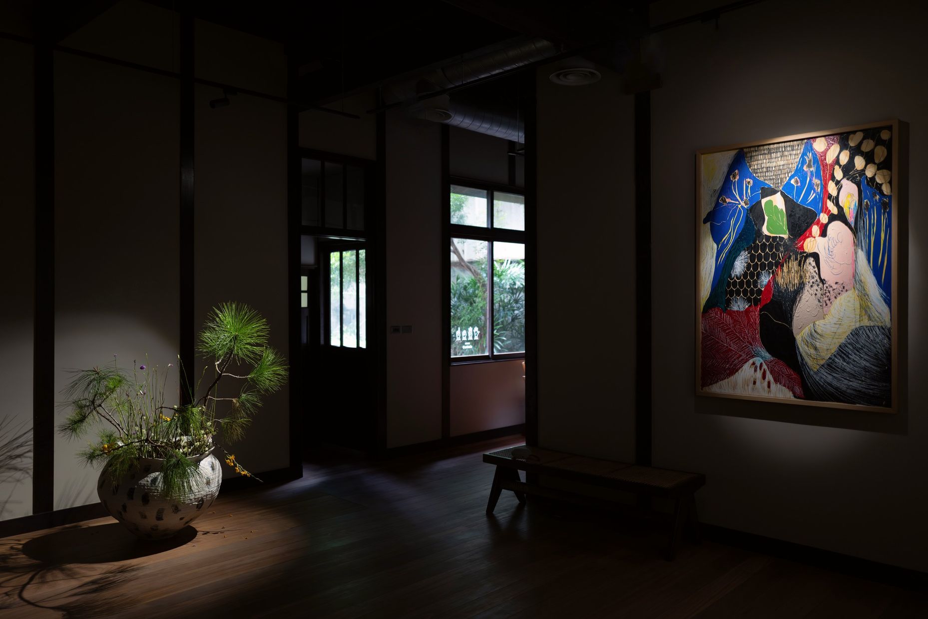 A pine and flower arrangement in a speckled jar on the floor, with Naotaka Hiro's painting on the far wall.