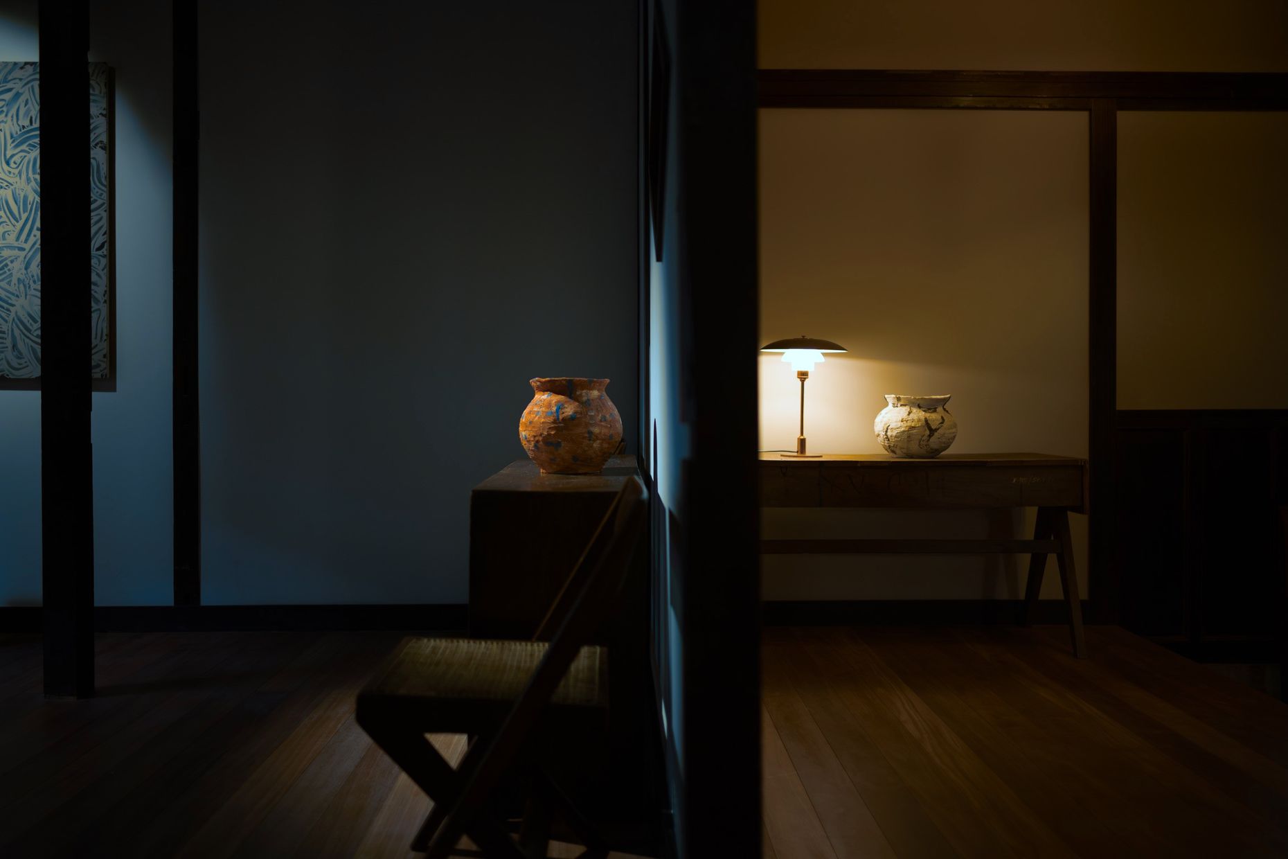 Two jars seen through a doorway, one on a pedestal and one on a desk under a lamp.