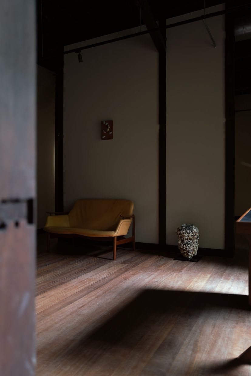 A long room seen past a wooden post: a sofa and a small panel on the far wall, and a mosaic vessel in the corner.
