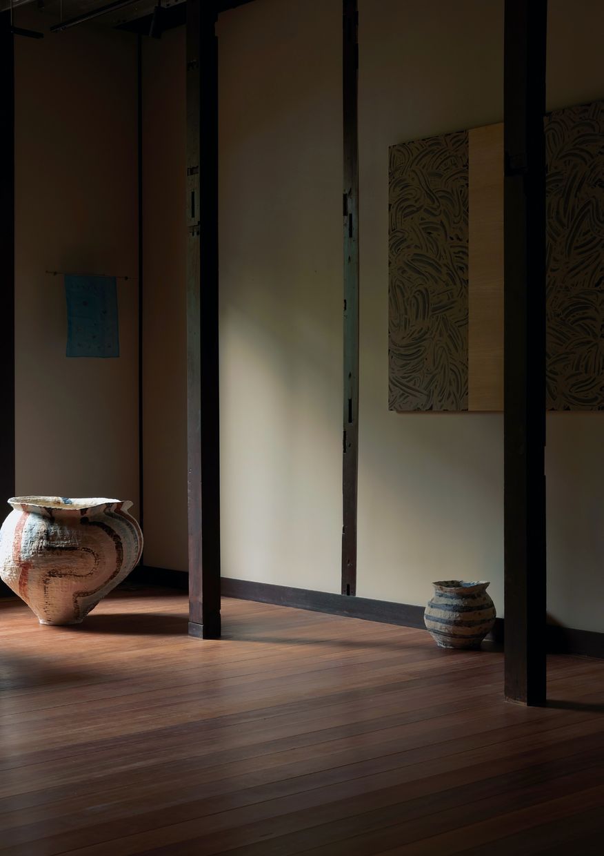 A dim room of the exhibition with ceramic jars on a wooden floor and works on the walls.
