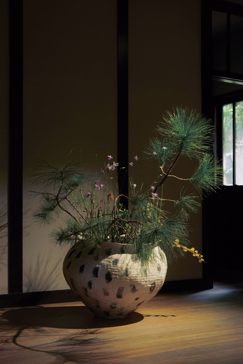 Pine branches and wildflowers arranged in a speckled ceramic jar.