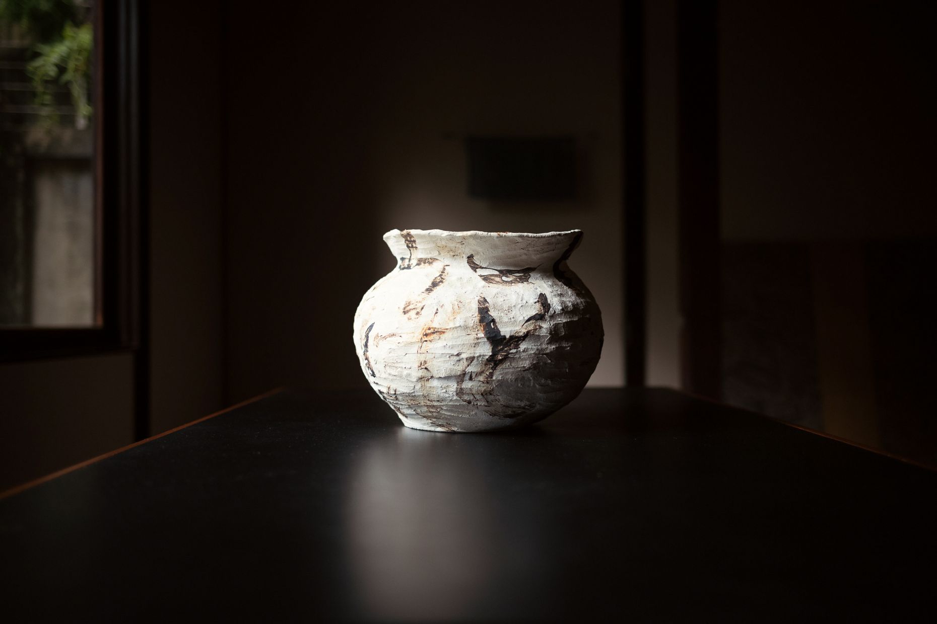 A white jar with brown and black marks on a black table in a dark room.
