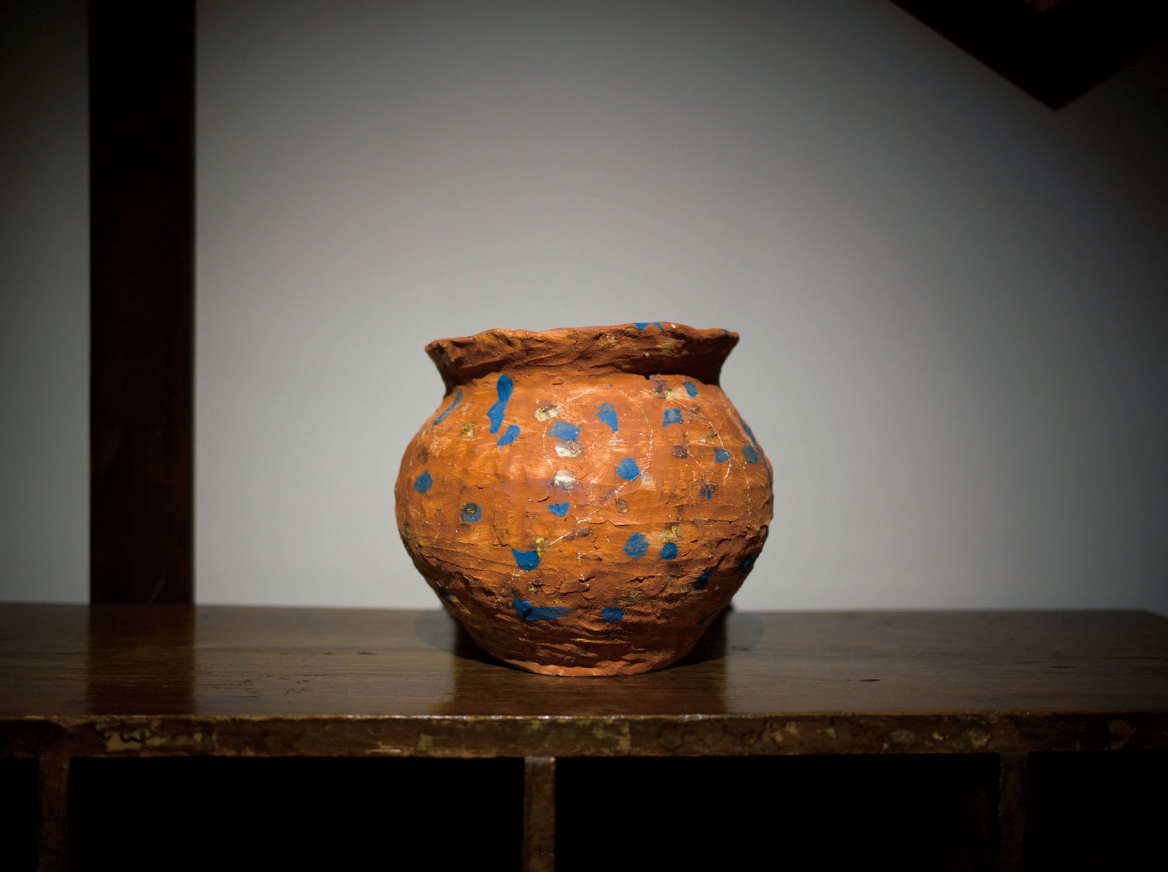 An orange jar with blue dots on an old wooden table.