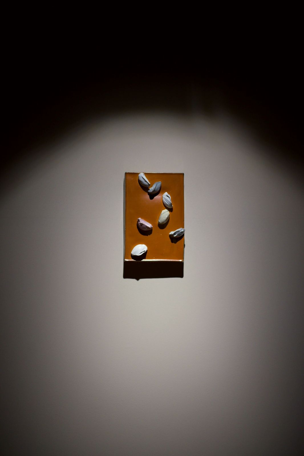 A small ceramic panel with pale shell-like forms, lit on a wall.
