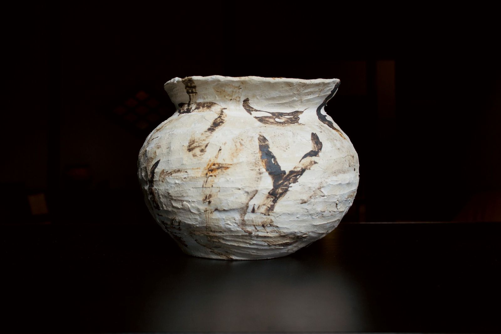 A white jar with brown and black marks on a black table in a dark room.