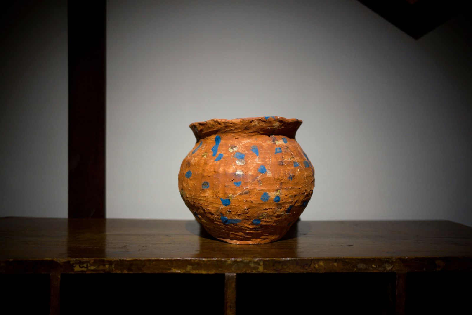An orange jar with blue dots on an old wooden table.