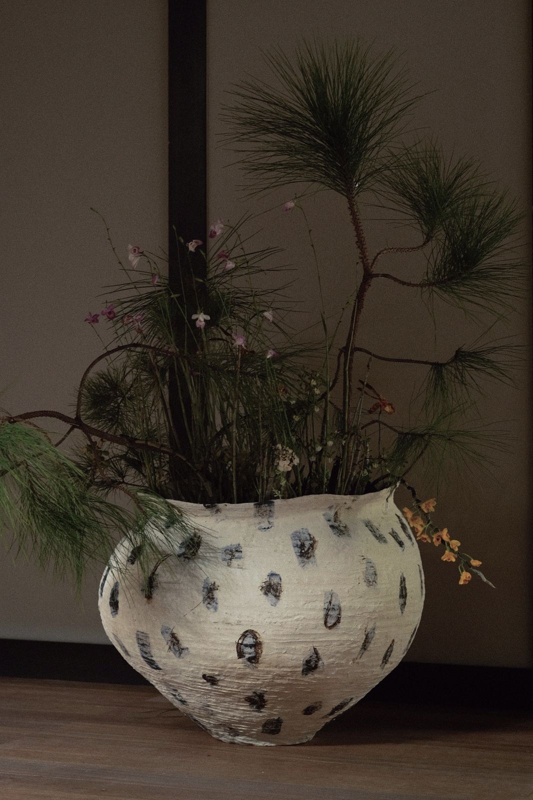 Pine branches and wildflowers arranged in a speckled jar on the floor.
