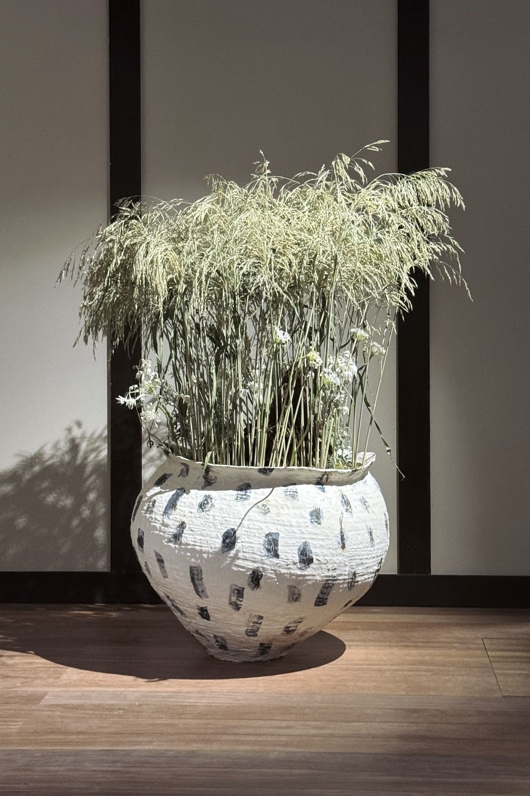Tall dried grasses in the speckled jar, with a beam of light on the floor.