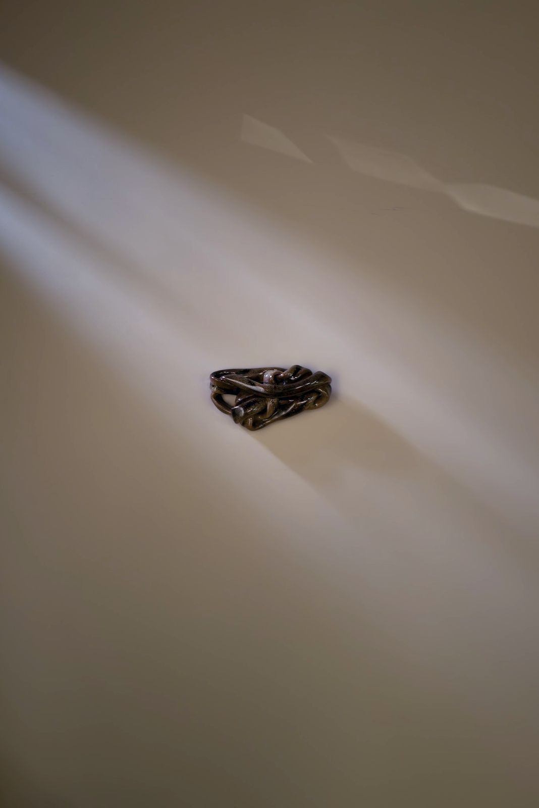 A small knotted ceramic form on a wall crossed by a beam of light.